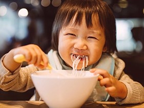 Een kind eet pasta uit een kom