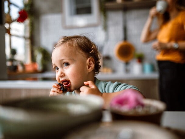 Un jeune enfant mange un aliment avec les mains dans la cuisine