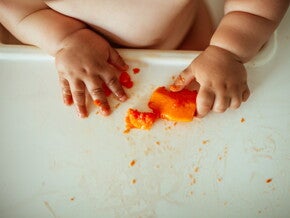 Un bébé attrape des morceaux de fruit avec ses doigts