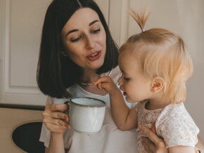 Mama houdt een kopje vast terwijl haar baby de rand aanraakt