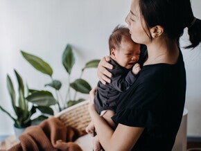 Une femme console un bébé qui pleure dans une pièce avec des plantes