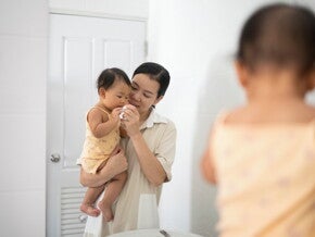 Un adulte tient un bébé devant le miroir de la salle de bain