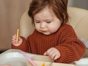 Un bébé assis dans une chaise haute mange une collation saine en regardant attentivement sa nourriture