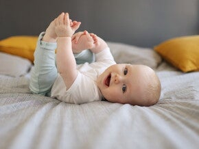 Baby ligt op bed en houdt zijn voeten vast terwijl hij lachend naar de camera kijkt