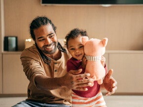 Vader speelt met lachende peuter die een knuffel vasthoudt