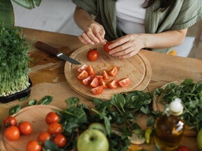 Een vrouw snijdt tomaten op een houten snijplank, omringd door groenten en verse kruiden