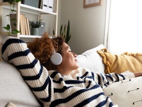 Een ontspannen vrouw luistert naar muziek met een koptelefoon terwijl ze op een sofa ligt.