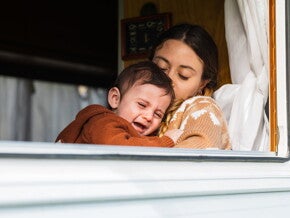 Une mère tient son bébé qui pleure et tente de le réconforter près de la fenêtre