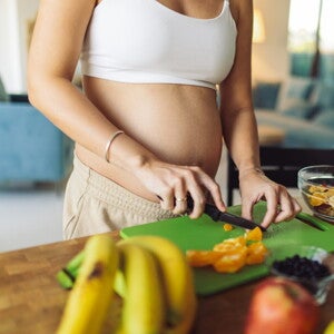 Femme enceinte coupe des fruits dans la cuisine