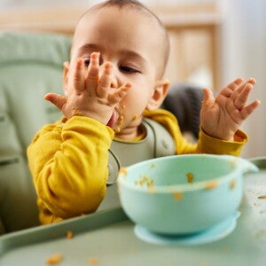 Bébé mange de la purée de légumes avec ses mains dans une chaise haute