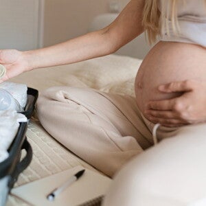 Une femme enceinte prépare une valise de maternité sur le lit