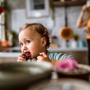 Un jeune enfant mange un aliment avec les mains dans la cuisine