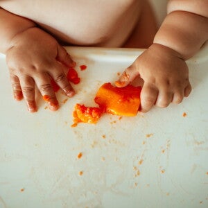 Un bébé attrape des morceaux de fruit avec ses doigts