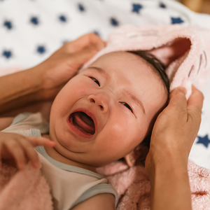 Photograph: crying baby wrapped in pink towel, adult hands gently cradling baby's head
