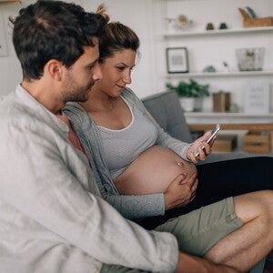 Toekomstige ouders die samen naar een smartphone kijken thuis, ter illustratie van Baby and Me Talk
