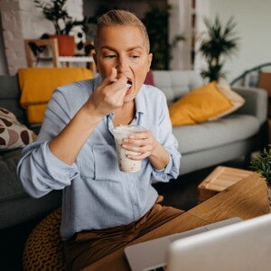 Personne mange un yaourt devant un ordinateur portable à la maison