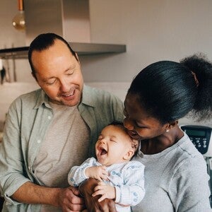 Photo: deux adultes souriants tenant un bébé riant dans une cuisine chaleureuse