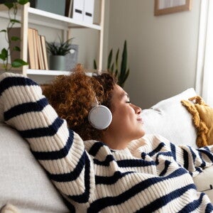 Une femme écoute de la musique avec un casque en étant allongée sur un canapé