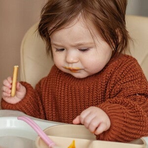 Un bébé assis dans une chaise haute mange une collation saine en regardant attentivement sa nourriture