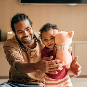 Vader speelt met lachende peuter die een knuffel vasthoudt