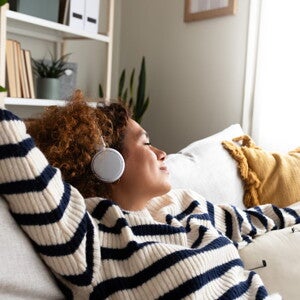 Une femme écoute de la musique avec un casque en étant allongée sur un canapé