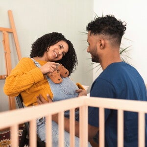 Zwangere vrouw die lachend baby­schoentjes op haar buik houdt terwijl haar partner voor haar knielt