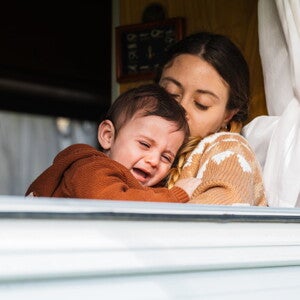 Une mère tient son bébé qui pleure et tente de le réconforter près de la fenêtre