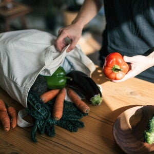 Une personne sort des légumes frais d’un sac de courses réutilisable sur une table en bois