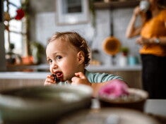 Un jeune enfant mange un aliment avec les mains dans la cuisine