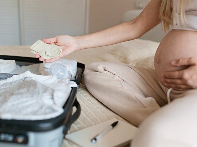 Zwangere vrouw die een ziekenhuiskoffertje inpakt op het bed