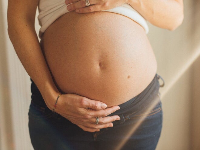 Zwangere vrouw die haar buik met beide handen ondersteunt