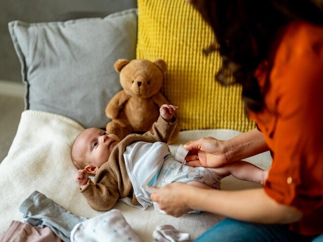 Femme change la couche d’un bébé sur un lit
