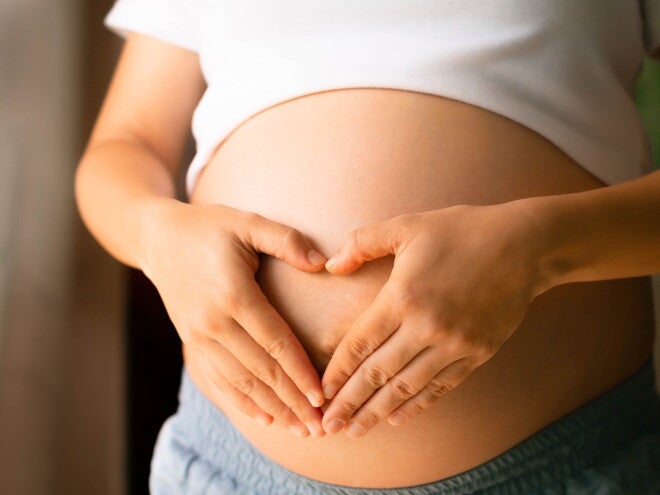 Zwangere vrouw vormt hart met haar handen op buik