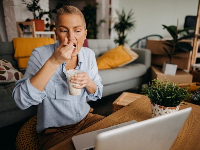 Personne mange un yaourt devant un ordinateur portable à la maison