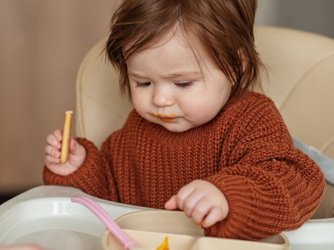 Un bébé assis dans une chaise haute mange une collation saine en regardant attentivement sa nourriture