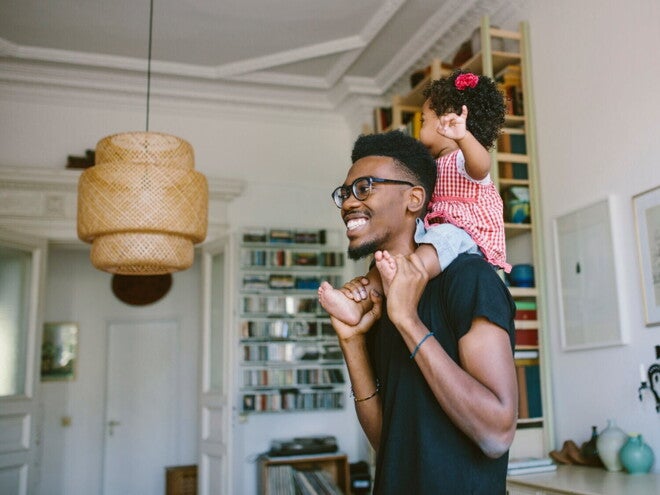 Un père porte son tout-petit en souriant sur ses épaules dans un salon chaleureux