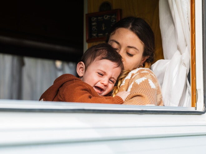 Moeder houdt een huilende baby vast en probeert hem te troosten bij het raam