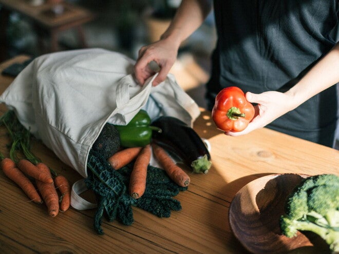 Une personne sort des légumes frais d’un sac de courses réutilisable sur une table en bois
