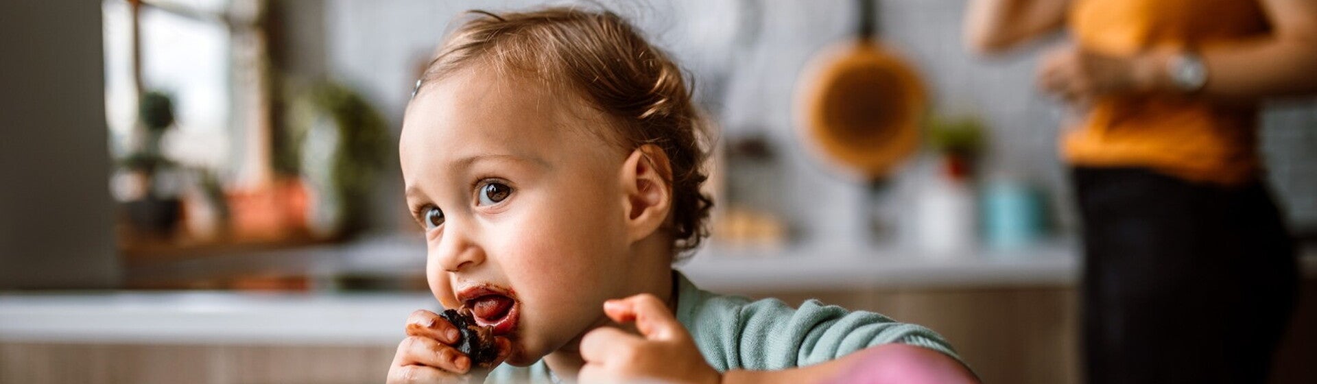Un jeune enfant mange un aliment avec les mains dans la cuisine