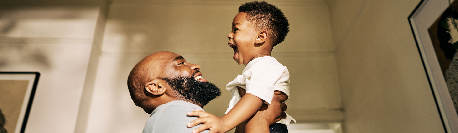 Photograph of smiling father lifting joyful toddler in sunlit room