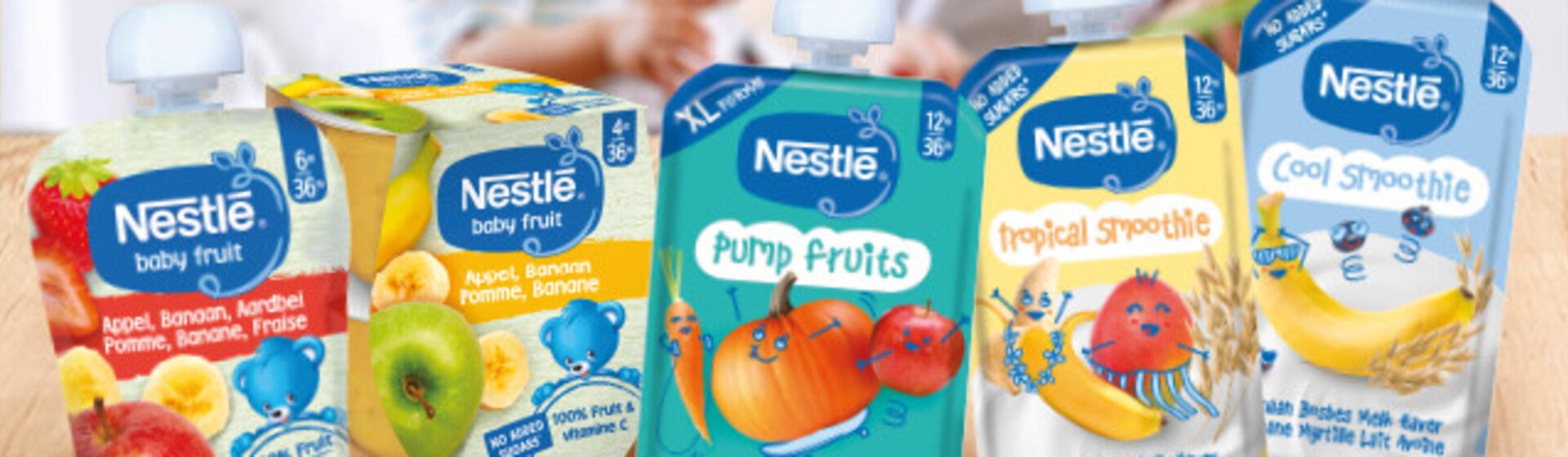 Un assortiment de sachets de nourriture pour bébé posés sur une table en bois, avec des silhouettes floues en arrière-plan.